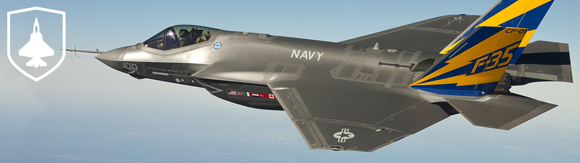 A U.S. Navy F-35 fighter jet with blue and yellow tail markings flies in clear skies; a white military jet emblem is visible on the left side of the image.