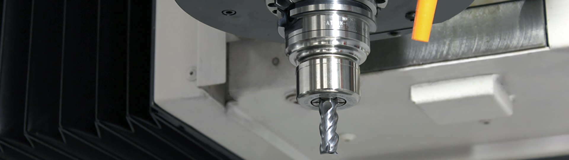 Solutions-Machining-Centers-hero_1920x542 Close-up view of a CNC tool holder holding a metal drill bit, with part of the machine’s interior and an orange coolant nozzle visible in the background.