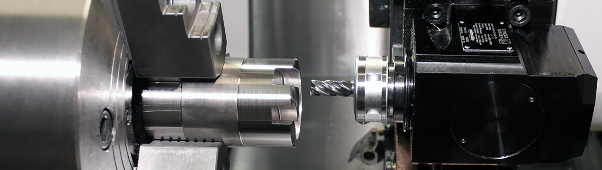 Solutions-Turning-Centers-hero_1920x542 A close-up view of a CNC milling machine with a Lyndex NIkken live tool cutting a cylindrical metal workpiece, with both the workpiece and the cutting tool held in precise alignment.