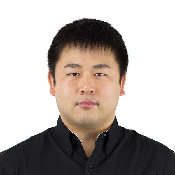 A man with short black hair and a neutral expression is facing forward. He is wearing a black collared shirt and is set against a plain white background.