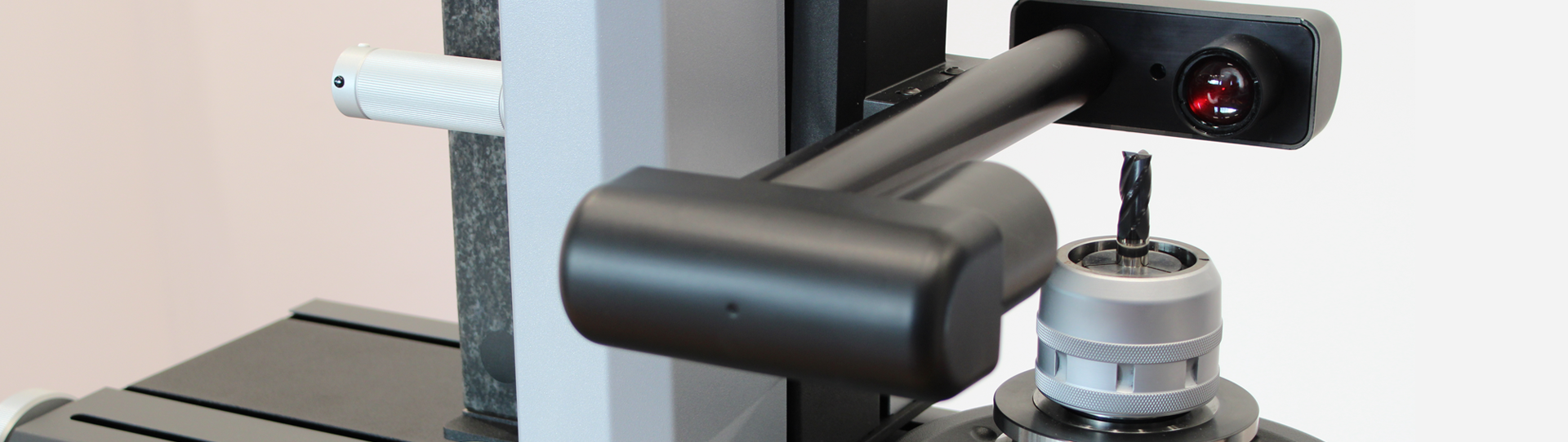A close-up of a precision measurement device inspecting a metal tool, possibly a drill bit, secured in a holder. The device includes a camera or sensor arm aimed at the tool for detailed analysis.