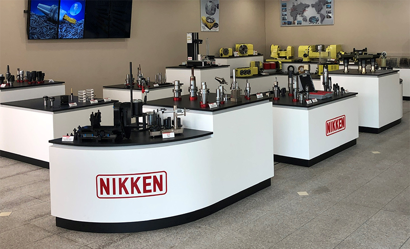 Nikken-Office-Showroom_800x486 Display counters in a showroom feature various industrial tools and machine components. The counters are white with the red NIKKEN logo. Yellow machinery and informational displays are visible in the background.