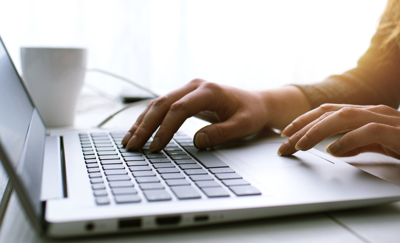 News-Media-Press-Releases_800x486 A person types on a silver laptop keyboard at a desk. A white coffee mug sits in the background, and natural light shines from the left side.
