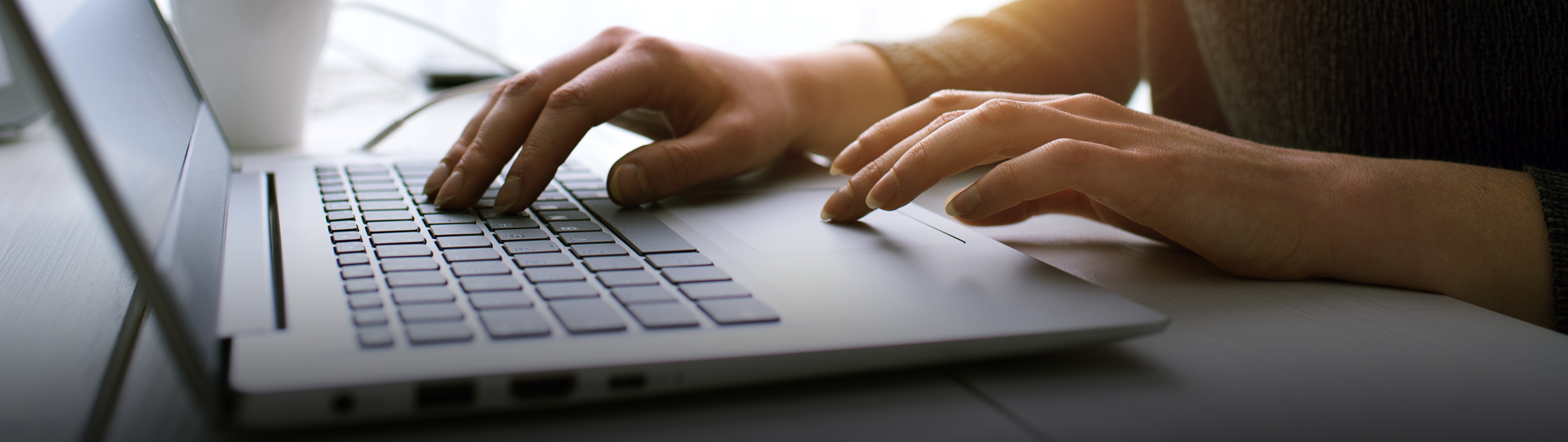 Press-Releases-Hero_1920x542 Close-up of a person’s hands typing on a laptop keyboard on a white desk, with natural light coming from a window in the background.