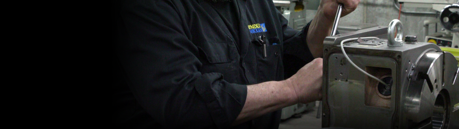 Service-and-Installation-Hero_1920x542_v2 A person in a dark work shirt is performing service, using a wrench to adjust a a Rotary Table body in an workshop setting. Tools and equipment are visible in the background.