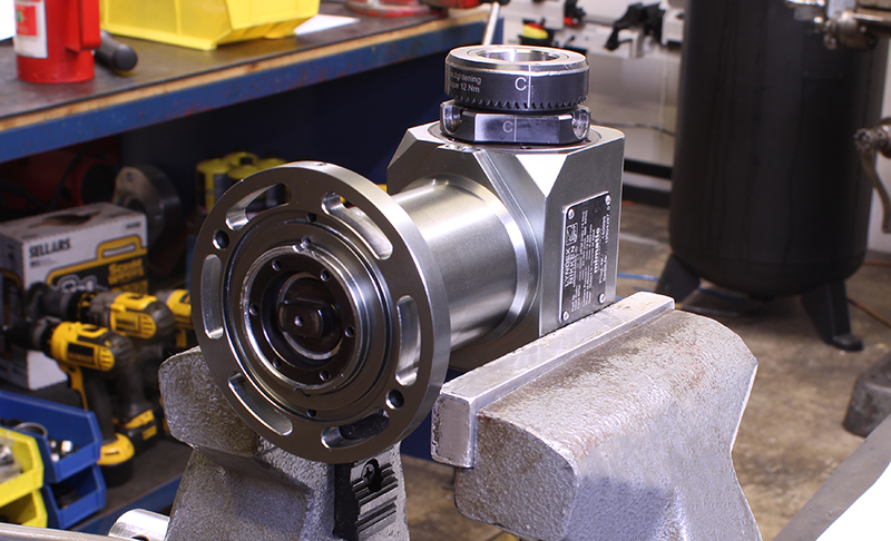 A close-up of an Angle Head secured in a vise, situated on a workbench in a workshop.