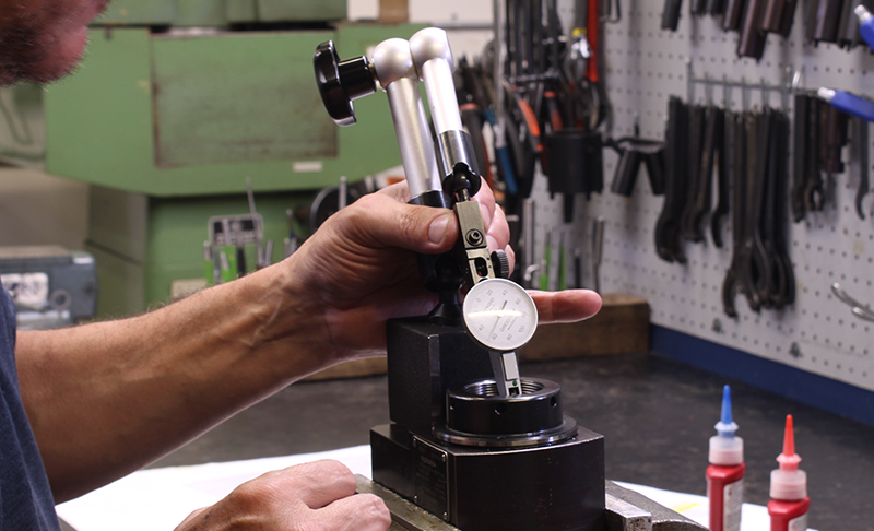 A person uses a dial indicator mounted on a magnetic base to measure precision of a metal part in a workshop.