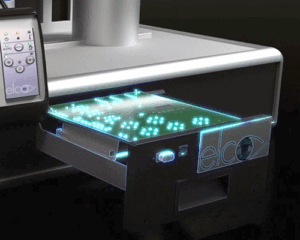 A close-up of an Fi6 Shrink Fit Machine with a glowing circuit board partially ejected from a compartment. The device has a control panel on the left and the brand name elco is visible on the front.