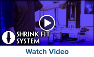 A person operates a shrink fit system machine in a workshop. The words SHRINK FIT SYSTEM appear on the left, and Watch Video is written at the bottom. A play button icon is centered over the image.