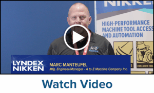 A man wearing a black shirt and red lanyard stands in front of a banner displaying High-Performance Machine Tool Access, Automation, and Clamping System. A play button icon is overlaid, with text below that reads, Watch Video.